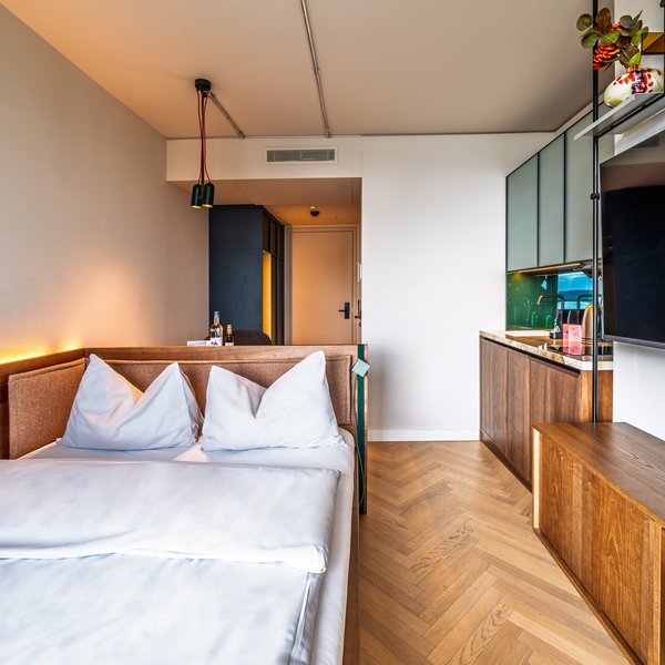 Perspektive vom Bett aus in das Apartment des The Zipper Hotels, inklusive TV-Wand und Einbauschränken aus Holz.