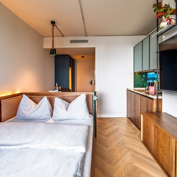Perspektive vom Bett aus in das Apartment des The Zipper Hotels, inklusive TV-Wand und Einbauschränken aus Holz.