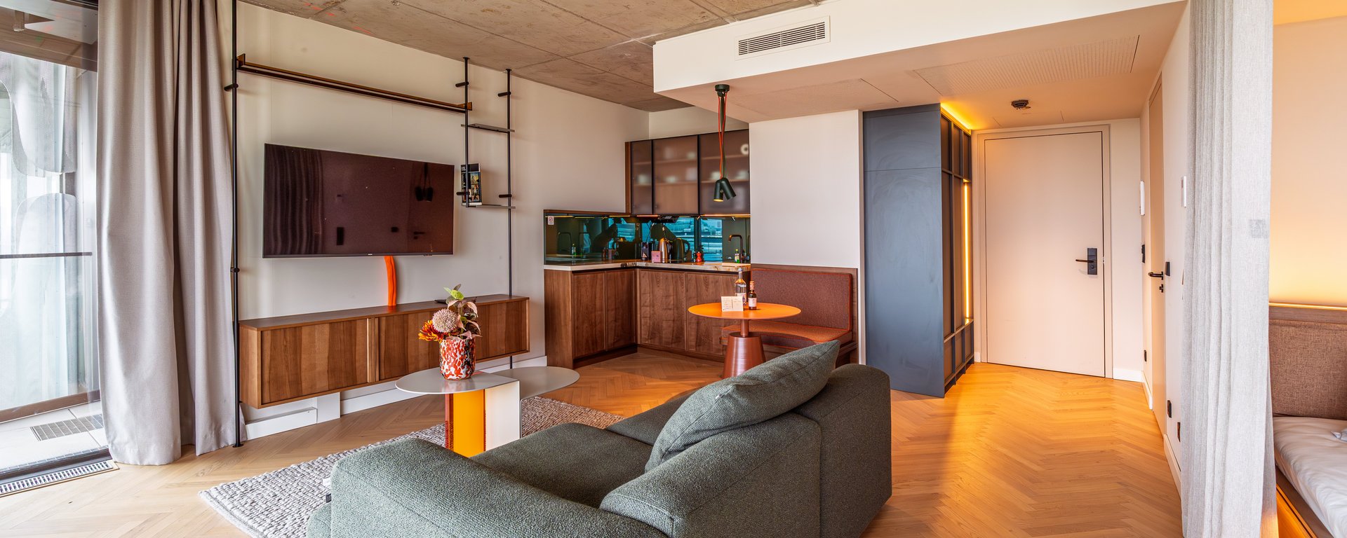 Offener Wohnbereich im The Zipper Apartment Home mit Parkettboden, modernem Sofa und TV-Wand.