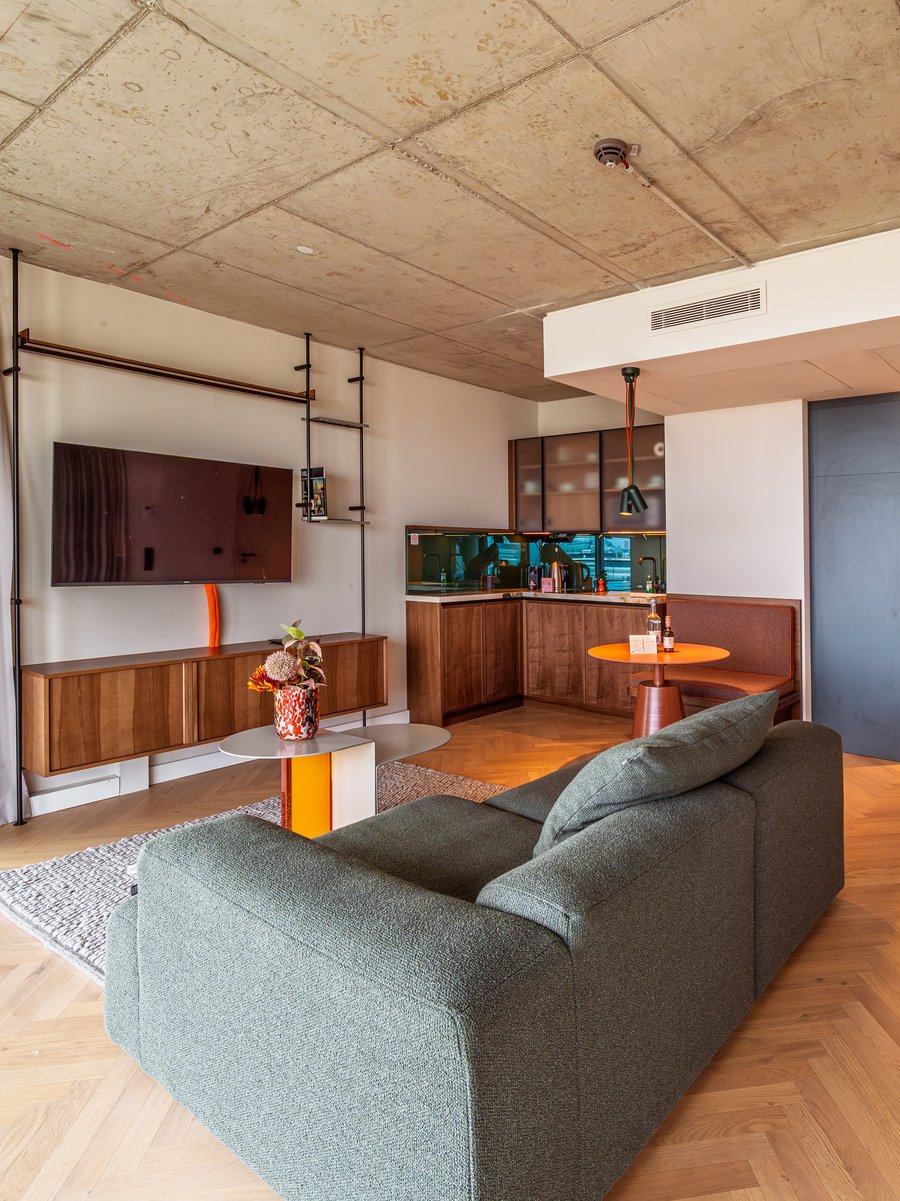 Offener Wohnbereich im The Zipper Apartment Home mit Parkettboden, modernem Sofa und TV-Wand.
