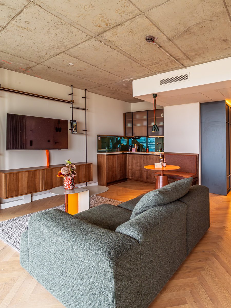 Offener Wohnbereich im The Zipper Apartment Home mit Parkettboden, modernem Sofa und TV-Wand.