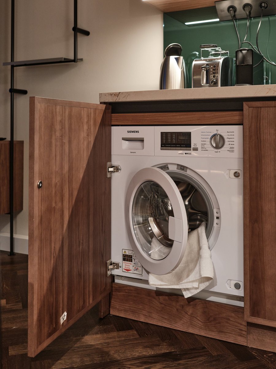 Offene Schranktür mit integriertem Waschtrockner in einem Apartment bei The Zipper Düsseldorf – ideal für Langzeitaufenthalte.