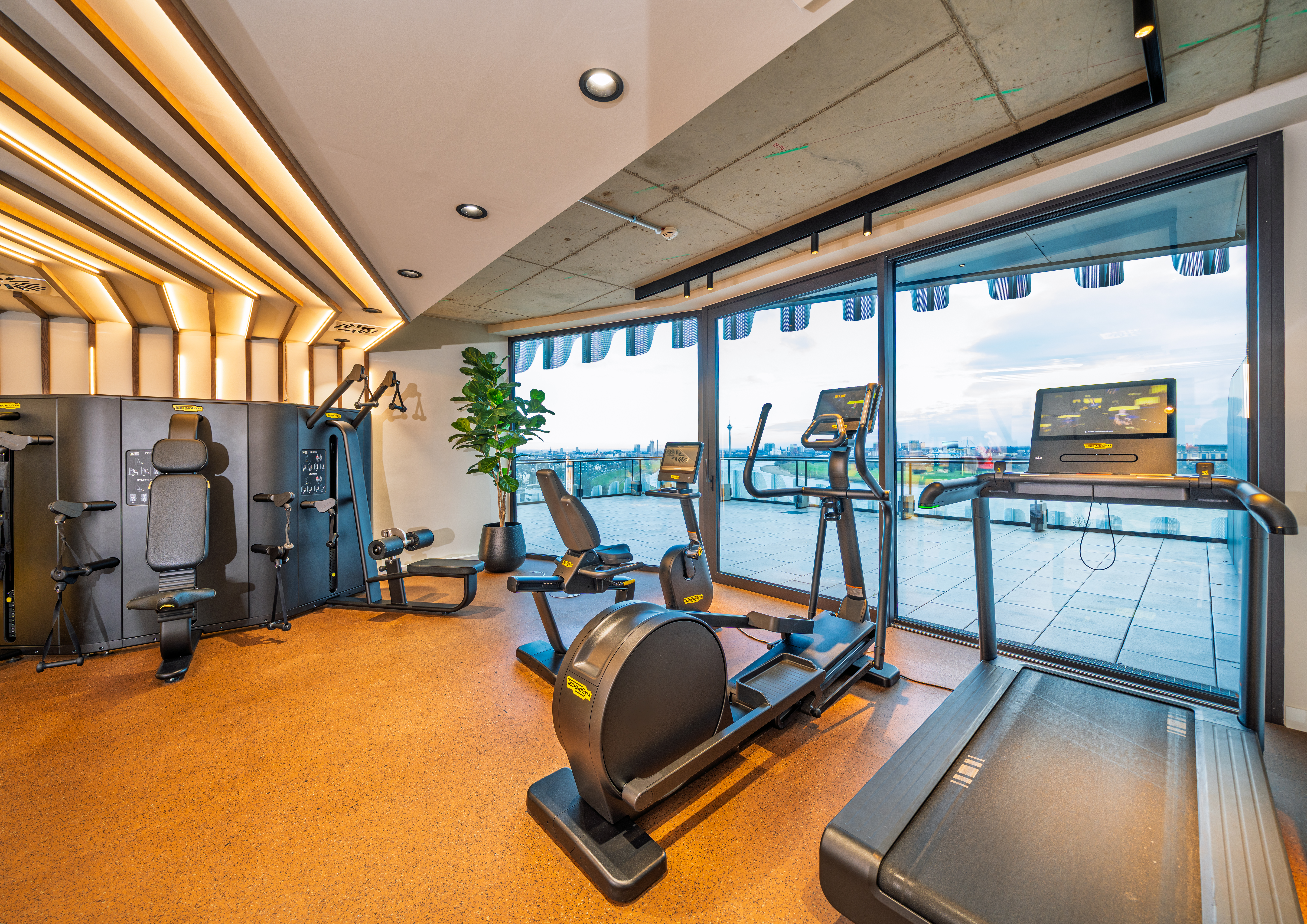 Modernes Gym im The Zipper Hotel mit Cardio-Geräten, Laufband und bodentiefen Fenstern für Training mit Aussicht.